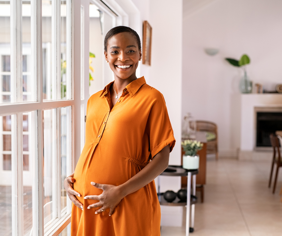 A glowing pregnant woman in orange dress holding her belly.