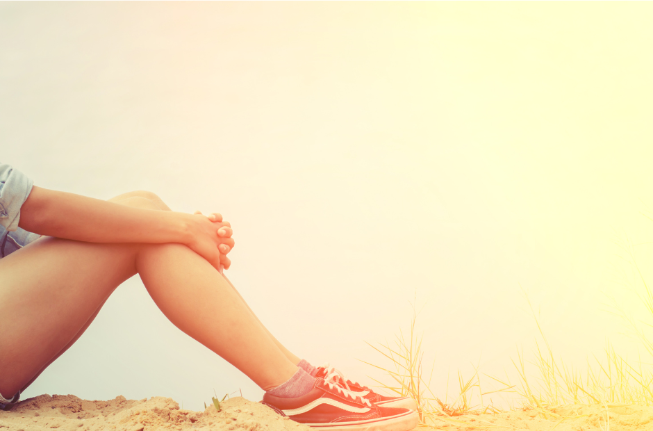 Woman experiencing endometriosis and sitting with arms around her legs on dirt ground in hues of yellow.